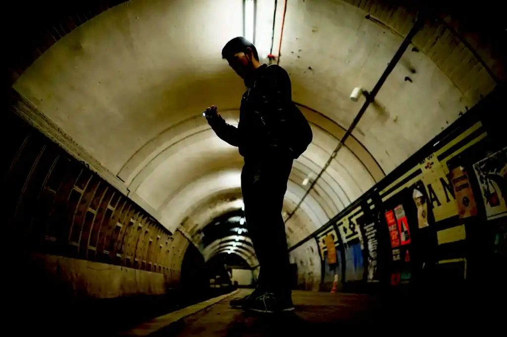 A lone visitor moves through a dimly lit, arched tunnel of London Underground Ghost Stations, with Aldwych Station style signage and walls.
