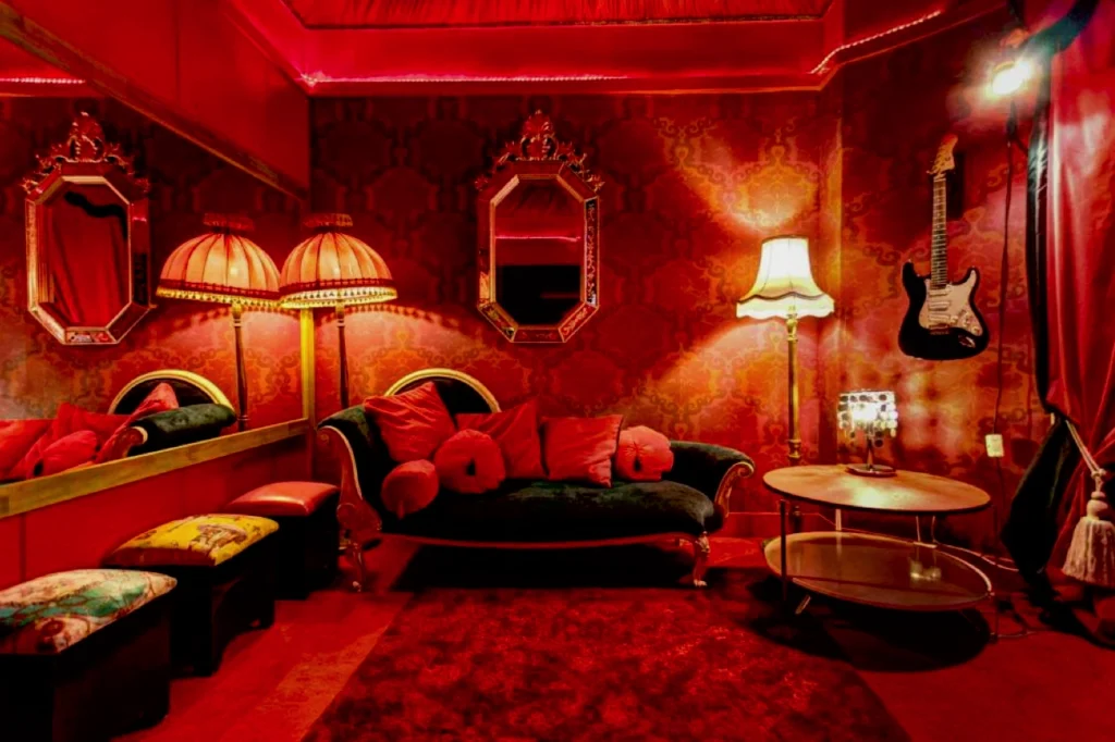 Inside Hotel Pelirocco, a neon-bright themed room with shocking pink-red walls, red velvet seating, mirrored panels and vintage-style lamps.