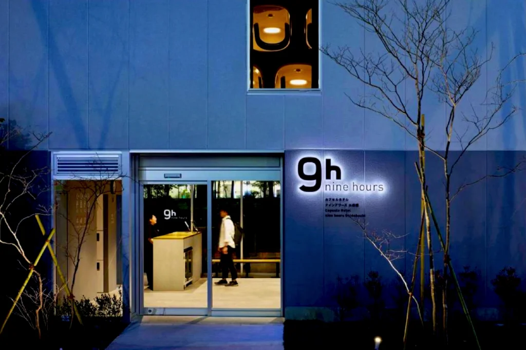 A blue night entrance for the Nine Hours Capsule Hotel, showing the lit 9h “nine hours” logo outside the capsule check-in area.