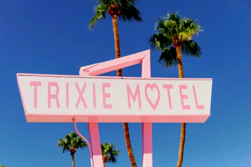 A bright pink TRIXIE MOTEL sign with heart-shaped lettering against a vivid blue sky, framed by palm trees in Palm Springs.