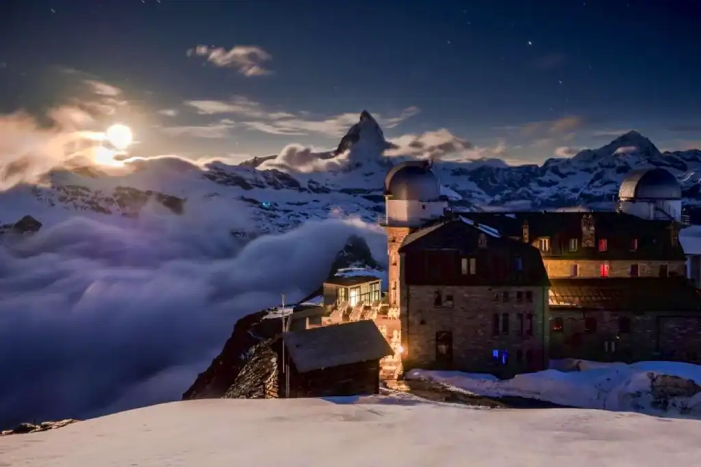 Night view of 3100 Kulmhotel Gornergrat at 3,100 metres in the Swiss Alps, with observatory domes above snowy clouds near the Matterhorn