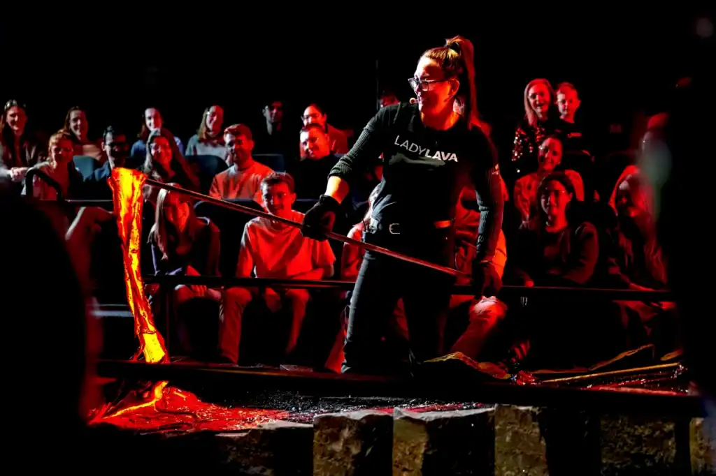 At Reykjavik Lava Show, spectators watch molten lava as it glows orange while “Lady Lava” handles it with a long metal rod indoors.