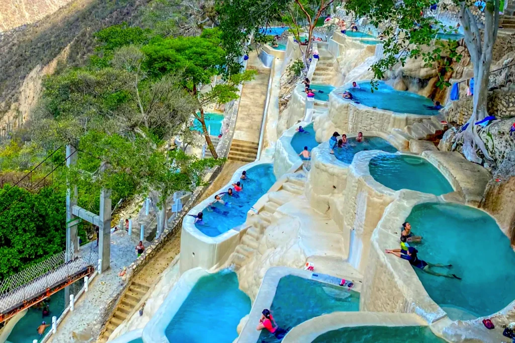 People wade through stepped pools of milky baby-blue thermal water at Tolantongo, with the canyon’s steep 500-metre walls rising around.