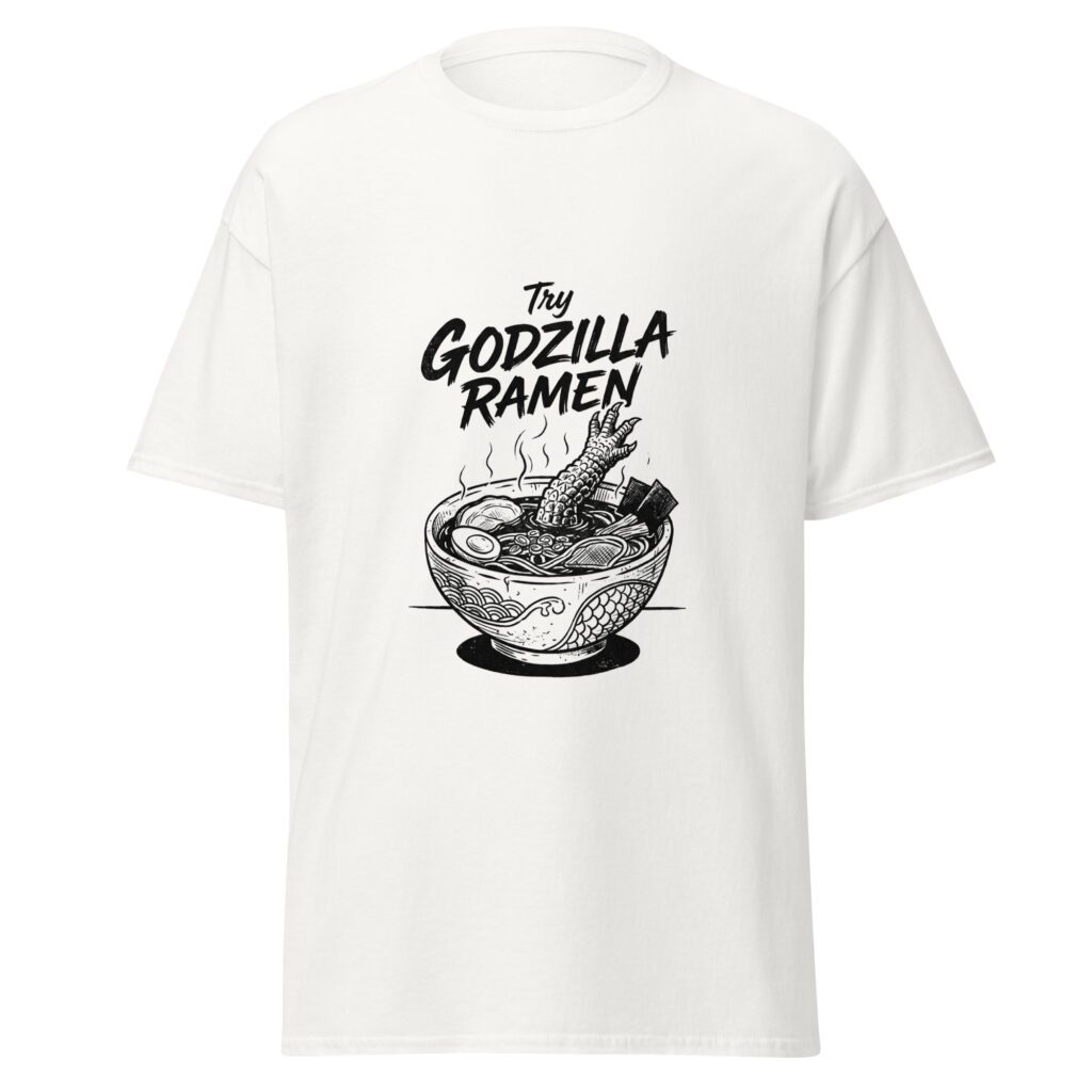 White t-shirt front with bold black “Try Godzilla Ramen” graphic, featuring steaming noodles and a clawed reptile leg in a ramen bowl.